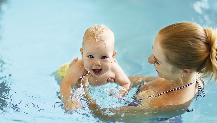 En mor holder smilende baby i vandet